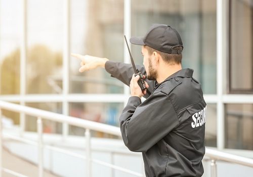 Male security guard using portable radio transmitter near building outdoors